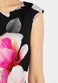 Ärmlös svart klänning med stora rosa och vita blommor samt mörkgrå blad på övre delen av bröstet och axeln.