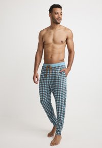 Mäns rutiga pyjamasbyxor i ljusblått med bruna rutor, med dragsko i midjan och smalnande anklar. Tillverkade av bomull.