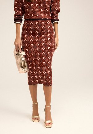 Femme portant un ensemble jupe et top marron à motif géométrique, tenant une pochette métallique, et portant des sandales à talons hauts dorées.