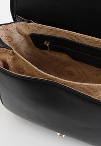 Svart läderhandväska med en krämig interiör, som har en dragkedjeficka och detaljer i guld. Slät textur och böjd form.