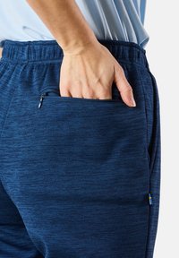 Marinblå träningsbyxor med en texturerad tyg. Har en sidficka med dragkedja och en liten svensk flagga som accent nära midjepartiet.