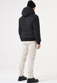 Schwarze Daunenjacke mit Kapuze, strukturierte Steppoptik, schmaler Schnitt und gerippte Bündchen, kombiniert mit hellen Hosen und schwarzen Stiefeln.