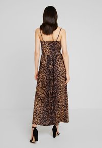 Robe longue à imprimé léopard marron et noir, fines bretelles, taille cintrée et tissu fluide, portée avec des chaussures à talons noires.