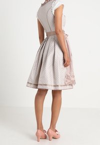 Robe gris clair avec un motif géométrique, manches courtes, taille ceinturée et ourlet orné de dentelle. Associée à des talons roses.