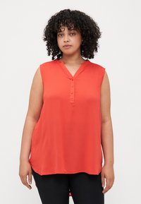 Blouse sans manches rouge avec un col en V, patte de boutonnage et coupe décontractée. Fabriquée en tissu léger avec une texture lisse.