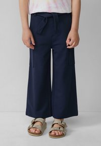 Marine wijd-uitlopende broek met een gestrikt tailleband en zijzakken, gecombineerd met lichte metallic sandalen met twee verstelbare gespen.