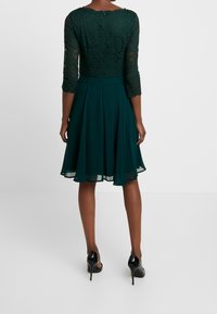 Grön spetsklänning med trekvartsärmar, utsvängd chiffongkjol och dragkedjedetalj bak. Slät textur med passande livstycke. Svarta klackar.