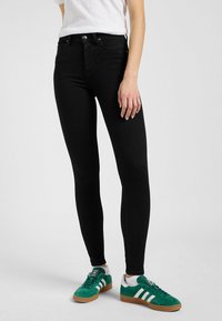 Črne ozke jeans hlače z visokim pasom, narejene iz denima. Imajo klasičen dizajn s petimi žepi in zadrgo z gumbom.