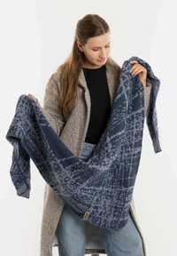 Écharpe en laine tricotée de couleur bleu foncé avec un motif texturé. Le matériau semble doux, mettant en valeur des nuances variées et une subtile étiquette de logo sur un bord.