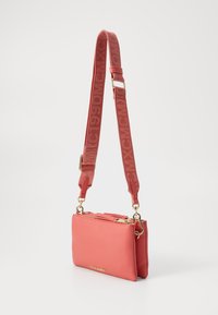 Coral crossbody bag made of textured leather, featuring a zippered top, gold hardware, and an adjustable strap with embossed branding.