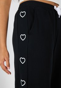 Svarta sweatpants med fyra vita hjärtramar längs sidosömmen och en vit dragsnodd i den elastiska midjebanden.