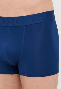 Temno modri bokserice iz teksturiranega materiala, z diskretnim logotipom na pasu in priležnim dizajnom z vidnimi šivi.