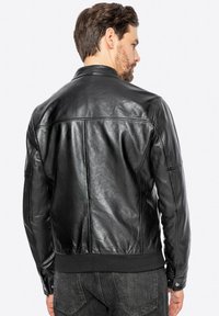 Chaqueta de cuero negra con un diseño ajustado, acabado texturizado y puños y cinturilla acanalados. Presenta un cuello clásico y detalles de costura.