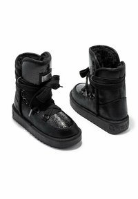 Las botas negras hasta el tobillo cuentan con un acabado en charol brillante, acentos de ante texturizado, gruesos cordones negros y un interior acolchado para mayor comodidad.