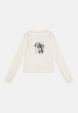 Hosszú ujjú krémszínű ing, középen balettcipő grafikával a mellkason. Puha anyag, kerek nyakkivágás, laza fazon.