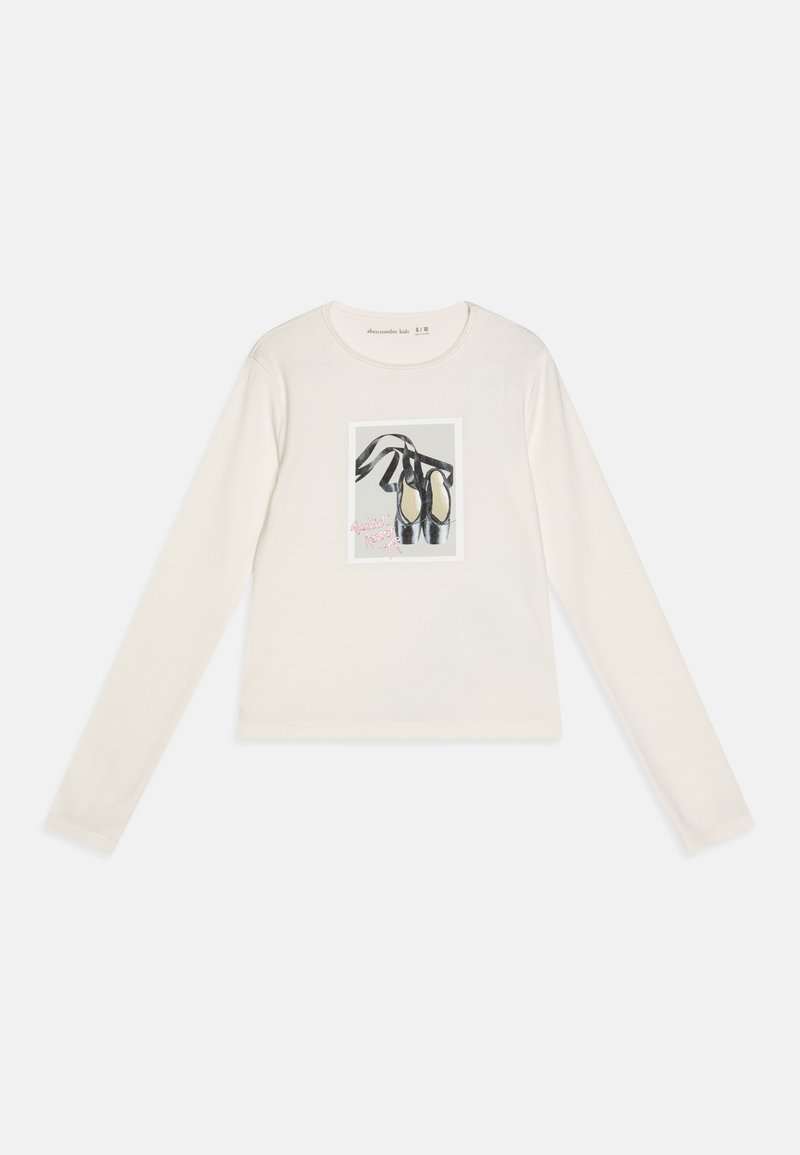 Camisa de manga larga color crema con un gráfico de zapatilla de ballet centrado en el pecho. Tejido suave, cuello redondo, ajuste casual.