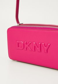 Fukszia bőr keresztpántos táska, dombornyomott "DKNY" logóval, cipzáras záródással és vékony lapos formával. Levehető vállpánttal rendelkezik.