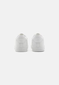 Hvit skinn sneakers med glatt finish, rund tå, lavt design, preget logo-detalj bak og teksturert gummisåle.