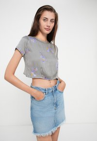 Top court à rayures avec broderie florale violette, associé à une jupe en denim taille haute avec un ourlet effiloché. Les deux présentent un style décontracté.