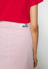 Punainen t-paita yhdistettynä vaaleanpunaiseen hameeseen. Hameessa on takapuolella "LOVE MOSCHINO" -labeli, hienovarainen pinta ja muotonsa mukainen istuvuus.