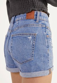 Pantalones cortos de mezclilla en azul claro con dobladillos, que cuentan con dos bolsillos traseros, un sutil desgaste y una etiqueta de cuero marrón en la cintura.