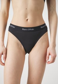 Culotte de bikini en coton noir avec une large taille élastique arborant le logo "Marc O'Polo". Texture lisse avec un design à taille haute.