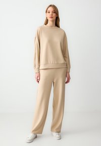 Beige katoenen sweatshirt en bijpassende wijde broek, met een ontspannen pasvorm, geribbelde manchetten en een gladde textuur, gecombineerd met witte sneakers.