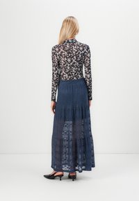 Top de manga larga a rayas en blanco y negro combinado con una falda maxi de encaje azul con volantes. La falda presenta una textura sutil y un diseño fluido.