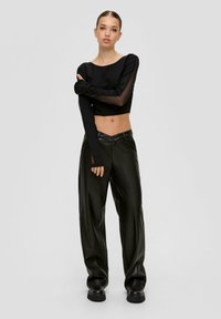 Schwarzes, kurzes Oberteil mit transparenten langen Ärmeln, kombiniert mit hoch taillierten, weit geschnittenen schwarzen Kunstlederhosen und klobigen schwarzen Stiefeln.