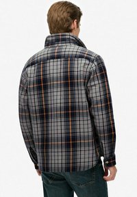 Flanellen shirt met een grijze basis, blauw en oranje ruitpatroon, met knoopmanchetten en een hoge kraag, van achteraf weergegeven.