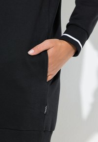 Felpa nera con tasca laterale, polsini a coste con dettagli bianchi e etichetta con logo sulla cucitura inferiore. Tessuto in cotone liscio.