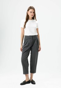 White short-sleeve top paired with gray tailored trousers featuring a cuffed hem. Black loafers with gold hardware accents. Smooth textures.