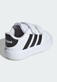 Zapatilla blanca con rayas negras y logo de la marca, que cuenta con un cuello acolchado y correas de Velcro. Parte superior de sintético suave y suela de goma.