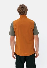 Orangenes ärmelloses Unterhemd aus leichtem Material, mit hohem Kragen und einem dezenten Logo am Saum, kombiniert mit einem grauen Kurzarmhemd.
