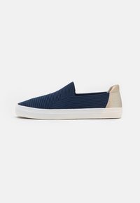 Chaussure slip-on marine avec tige en textile côtelé, semelle en caoutchouc blanche et accent de talon beige clair. Présente un design minimaliste sans lacets.