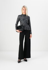 Long-sleeve, fitted top in black and gray leopard print, paired with wide-leg black trousers and a textured black handbag. Black pointed shoes.