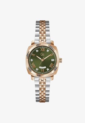 Zlaté a strieborné dvojvstvové hodinky s osmihranným puzdrom, zeleným ciferníkom, diamantovými akcentmi a rímskymi číslicami. Zobrazenie dňa na 6. hodine.