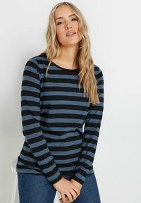 Långärmad T-shirt med horisontella svarta och blå ränder, rund halsringning och mjukt tyg, kombinerad med avslappnade blå jeans.