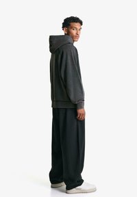 Gray oversized hoodie with a drawstring hood, paired with loose black trousers and white sneakers. Smooth fabric texture and relaxed fit.