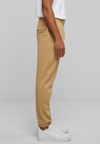 Beige Jogginghosen aus weichem Stoff, mit einem elastischen Bund, seitlichen Taschen und gerippten Bündchen, kombiniert mit weißen Sportschuhen.