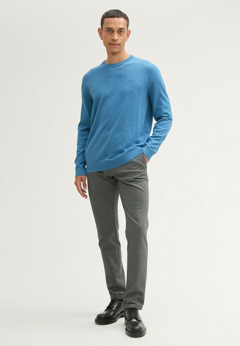 Maglione a maniche lunghe blu in maglia abbinato a pantaloni grigi su misura e scarpe nere stringate. Texture liscia con una vestibilità rilassata.
