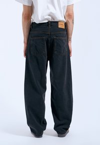 Black denim wide-leg jeans with a high waist, five pockets, and a brown leather label at the back. Contrast stitching detail visible.