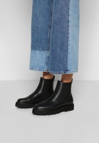 Black leather Chelsea boots with elastic side panels, thick rubber sole, rounded toe, and textured surface, paired with a denim skirt.