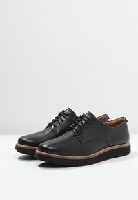 Chaussures en cuir noir avec une surface texturée, un bout arrondi et un design à lacets. Comprennent une semelle marron clair contrastante avec des accents de surpiqûres.