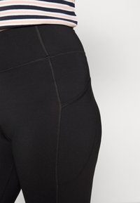 Leggings pretos de cintura alta com uma textura suave, apresentando costuras em contraste e um detalhe de bolso lateral. Ideais para vestuário ativo.