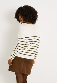 Jersey de rayas en crema y oliva, de corte holgado con mangas largas, combinado con una minifalda de ante marrón y medias opacas.