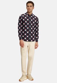 Schwarze Button-Up-Hemd mit einem festlichen weißen und roten Santa-Druck, kombiniert mit cremefarbenen Hosen und hellen Sneakern.