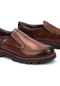 Zapatos marrones de cuero tipo slip-on con paneles elásticos en los laterales, detalles de costura y suela de goma texturizada. Acabado suave con punta redondeada.