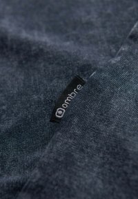 Tmavě modrá látka s texturovaným povrchem, obsahující černou etiketu s bílým písmem, částečně složenou, aby bylo vidět materiál.