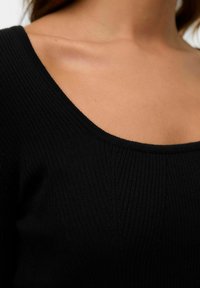 Top en tricot noir à côtes avec un large col en rond, présentant un motif texturé et une coupe ajustée.